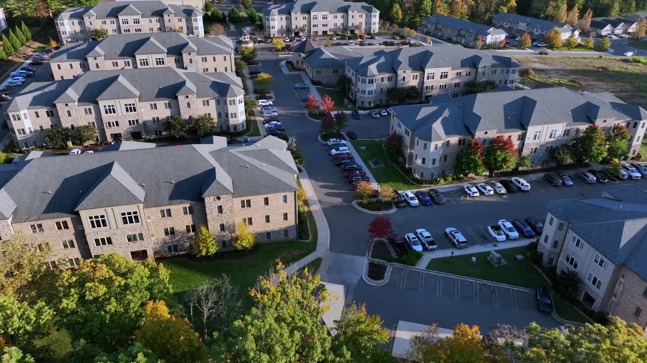 Aerial top down of new build apartment complex in suburb neighborhood. American city during sunny autumn day. Descend shot. Parking cars on parking lot. Colorful trees along street. Virginia, USA.