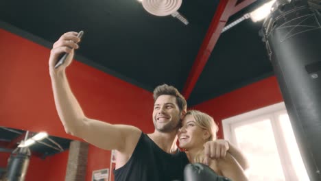 Embracing-fitness-couple-posing-to-mobile-phone-for-selfie-in-gym-club.