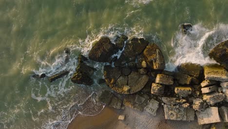 Beautiful-aerial-birdseye-view-of-Karosta-concrete-coast-fortification-ruins,-vibrant-sunset-over-stormy-Baltic-sea,-winter-evening,-slow-motion-drone-orbit-shot