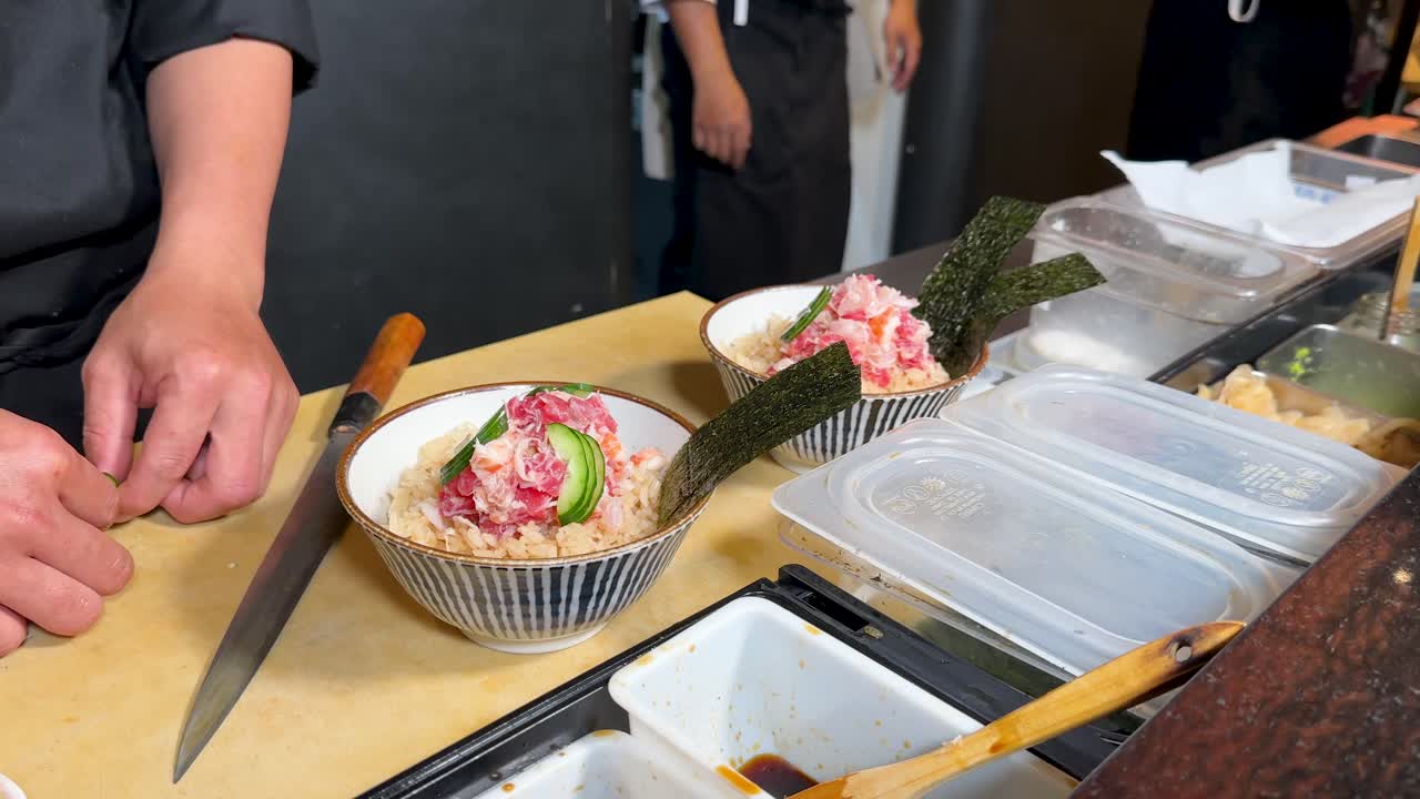 Close-up shot of a chef's hands garnishing sashimi rice bowls in a professional kitchen