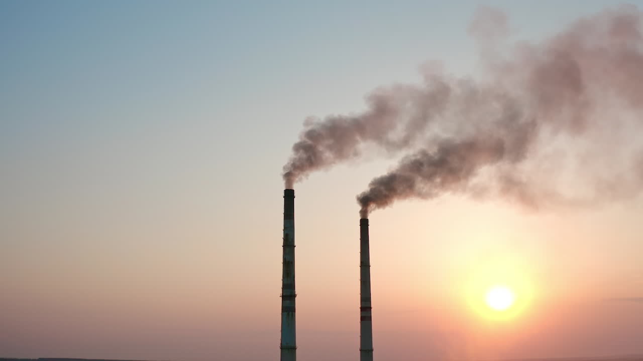 Smoke pipes on clear evening sky background. Factory chimneys release dark emissions into the atmosphere. Chemical smoke pollute the air. Ecology in danger.