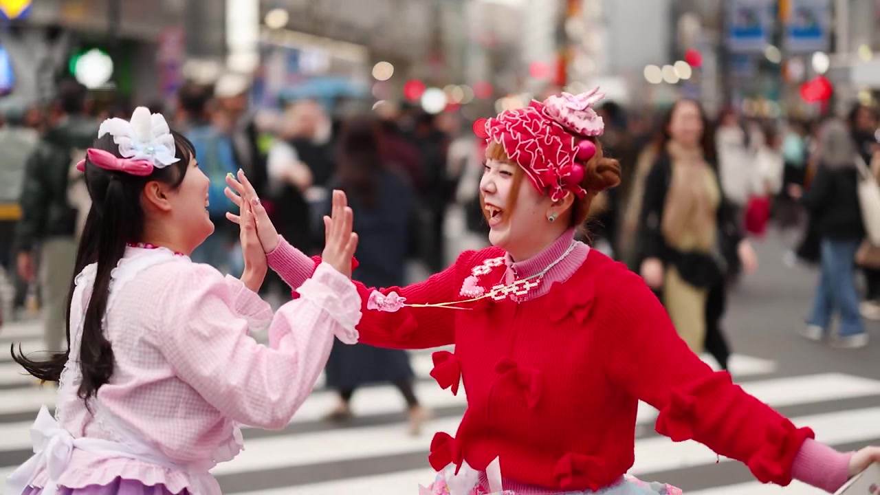 Jovens mulheres com vibrante estilo de rua japonês cumprimentam-se com um high five em um movimentado cruzamento de Tóquio.