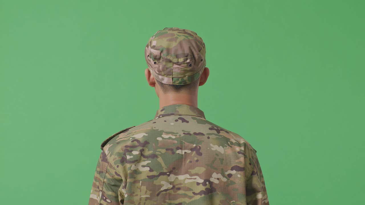 Close-up da parte de trás de um soldado asiático olhando ao redor enquanto está em pé no estúdio com fundo verde.