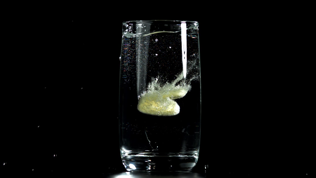 Compressa effervescente che cade in un bicchiere d'acqua al rallentatore