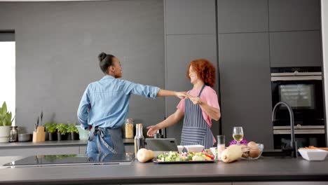 happy diverse couple in aprons having fun cooking and dancing together in kitchen, in slow motion