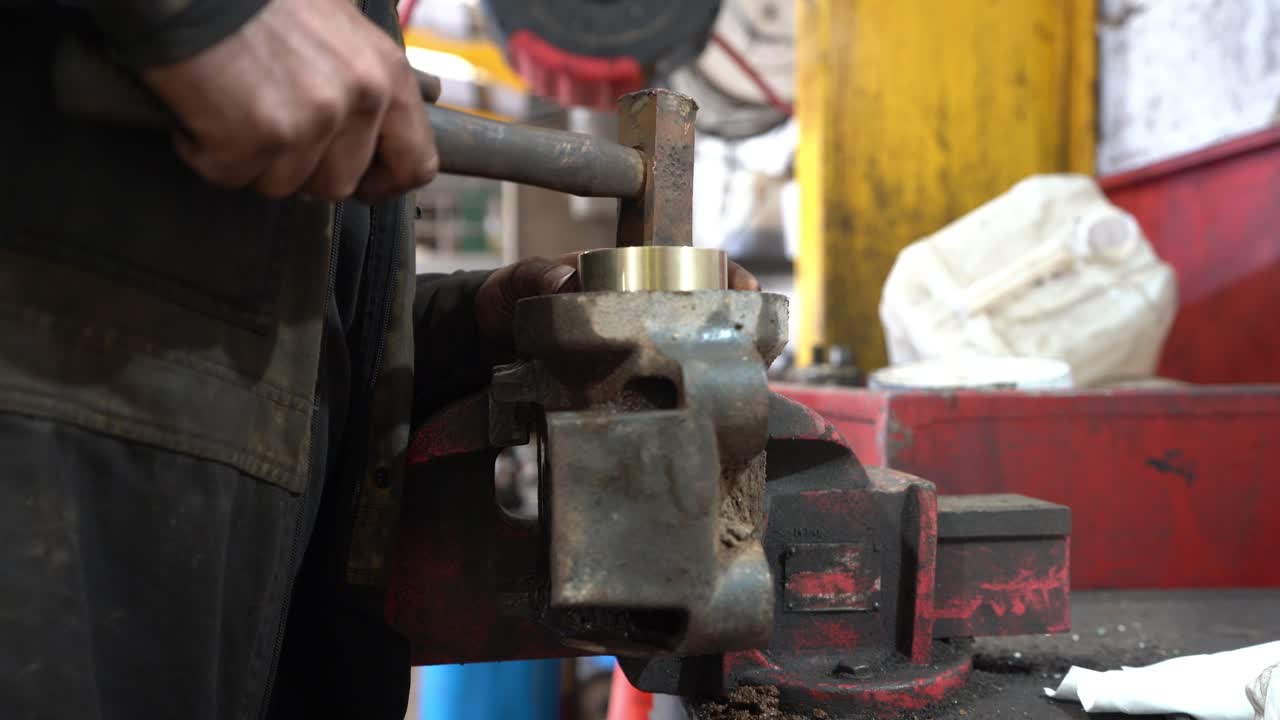 A mechanic with dirty hands in his workshop hammering home a brass bush into a housing held tightly in an engineer's vice