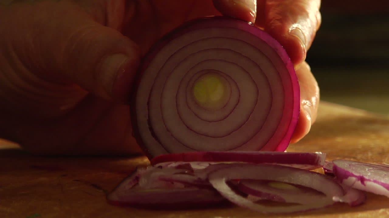 un hombre corta una cebolla roja en una tabla de cortar