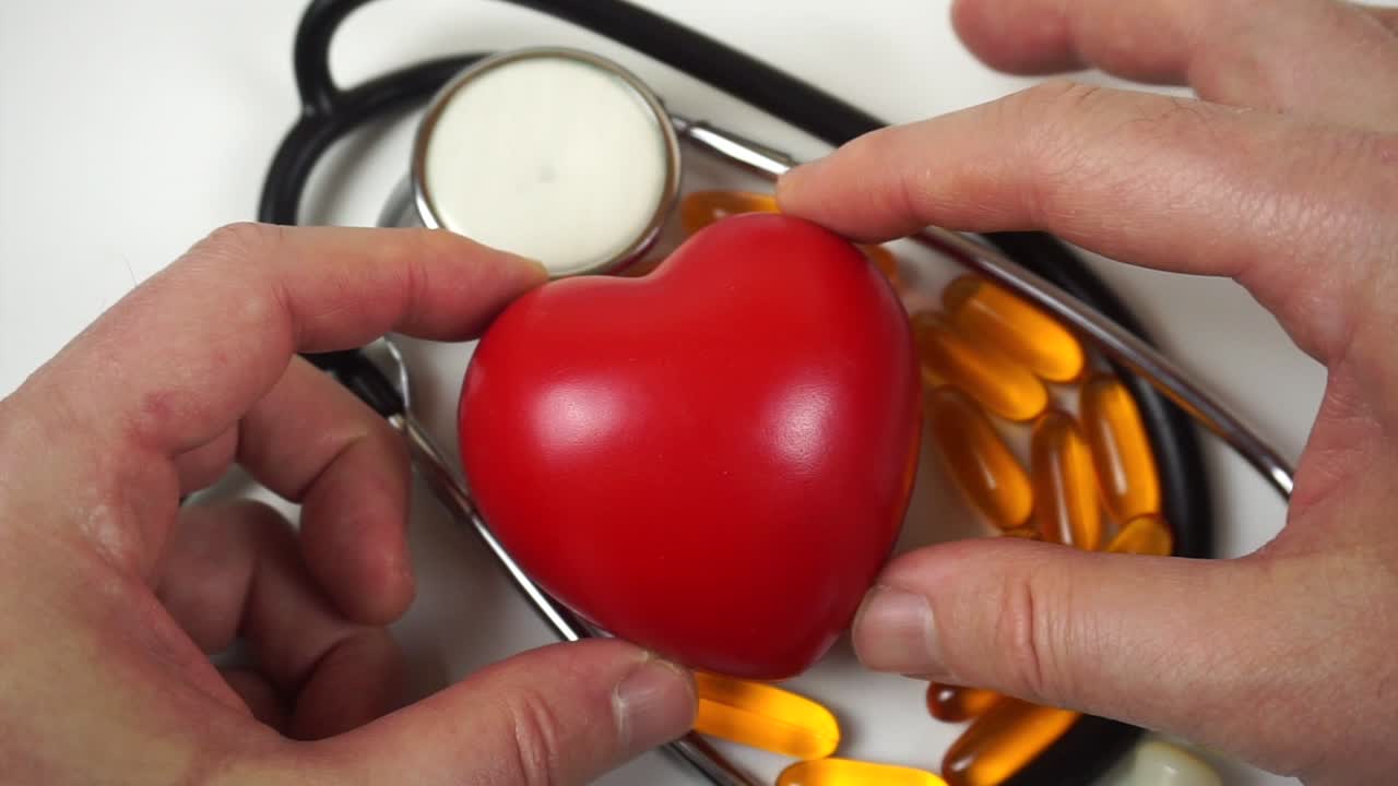 Doctor's hands placing a heart symbol on pills and a stethoscope on a white background