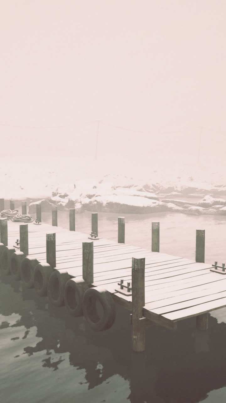 Snowy dock extends into foggy waters near a quiet cabin in winter