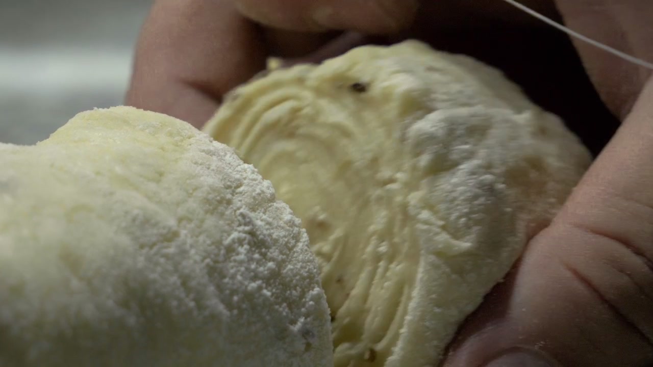 Bread dough is slowly cut with a thread. Back angle.