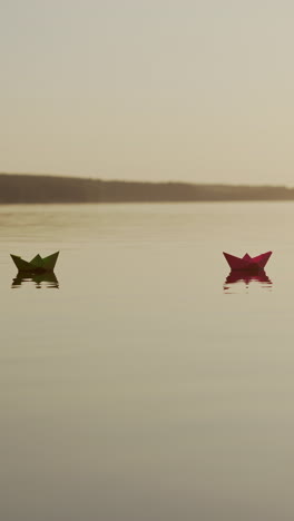 paper boats swim at sunset. evening water background and two origami ships floating. dreams and future concept. vertical video