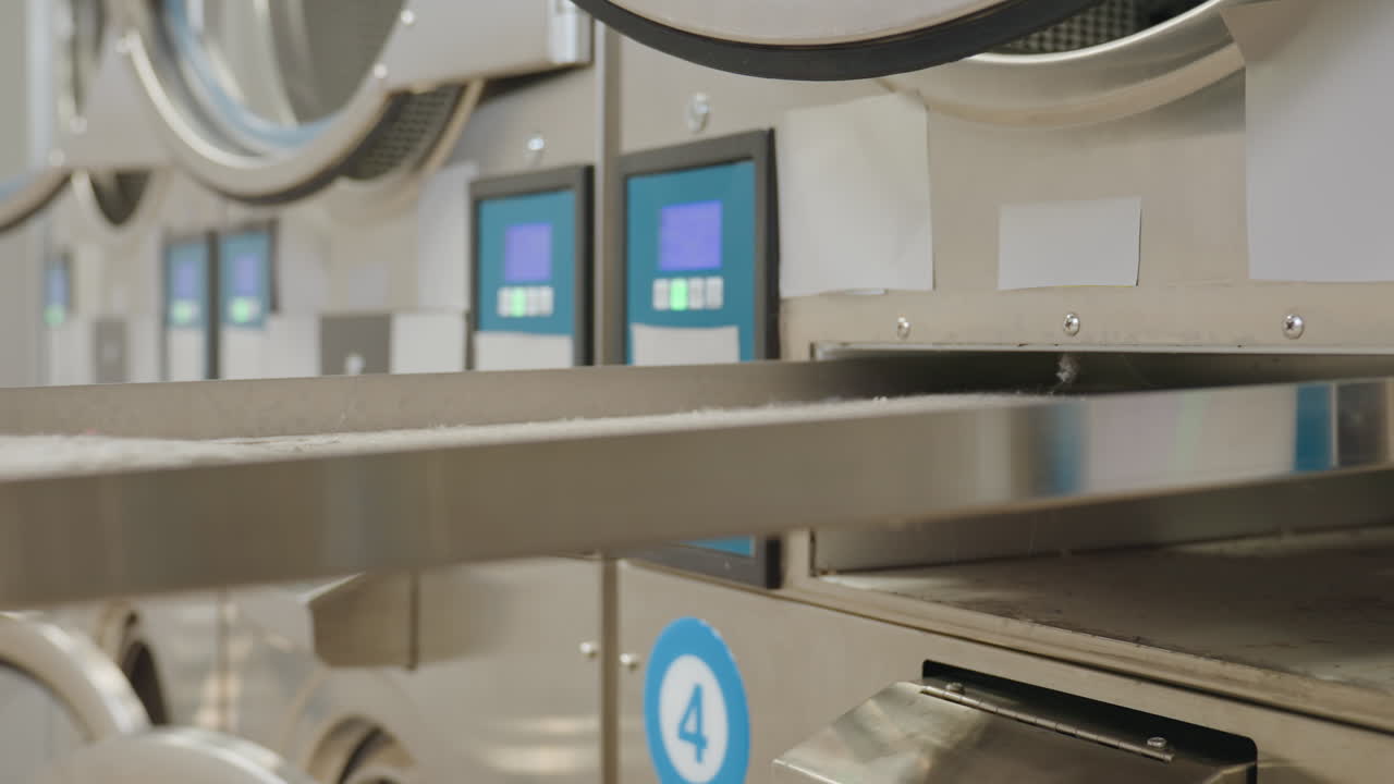 Industrial washing machine with electronic control panels as female hand inserts key into drawer lock and pulls it out, showing operation and maintenance process in laundromat facility