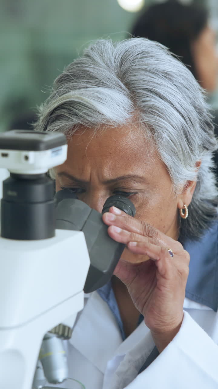 Scienziato anziano concentrato che osserva attraverso un microscopio in un laboratorio.