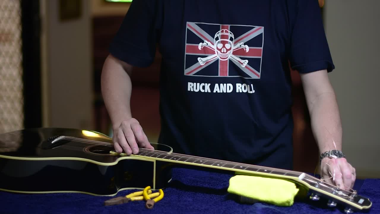 Restringing and cleaning a beautiful black single cutaway accoustic guitar - tensioning the strings by turning the machine heads and removing the excess stings with snips