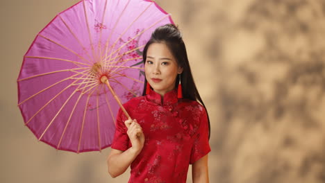 portrait shot of asian young cheerful woman in red traditional clothes holding parasol while smiling at camera