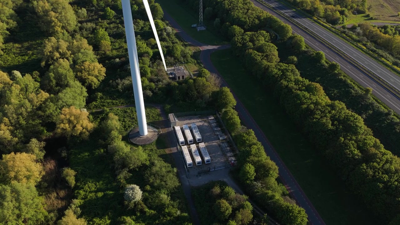 Aerial view of a battery storage system beside a wind turbine, showing renewable energy storage, grid support, and sustainable power infrastructure.