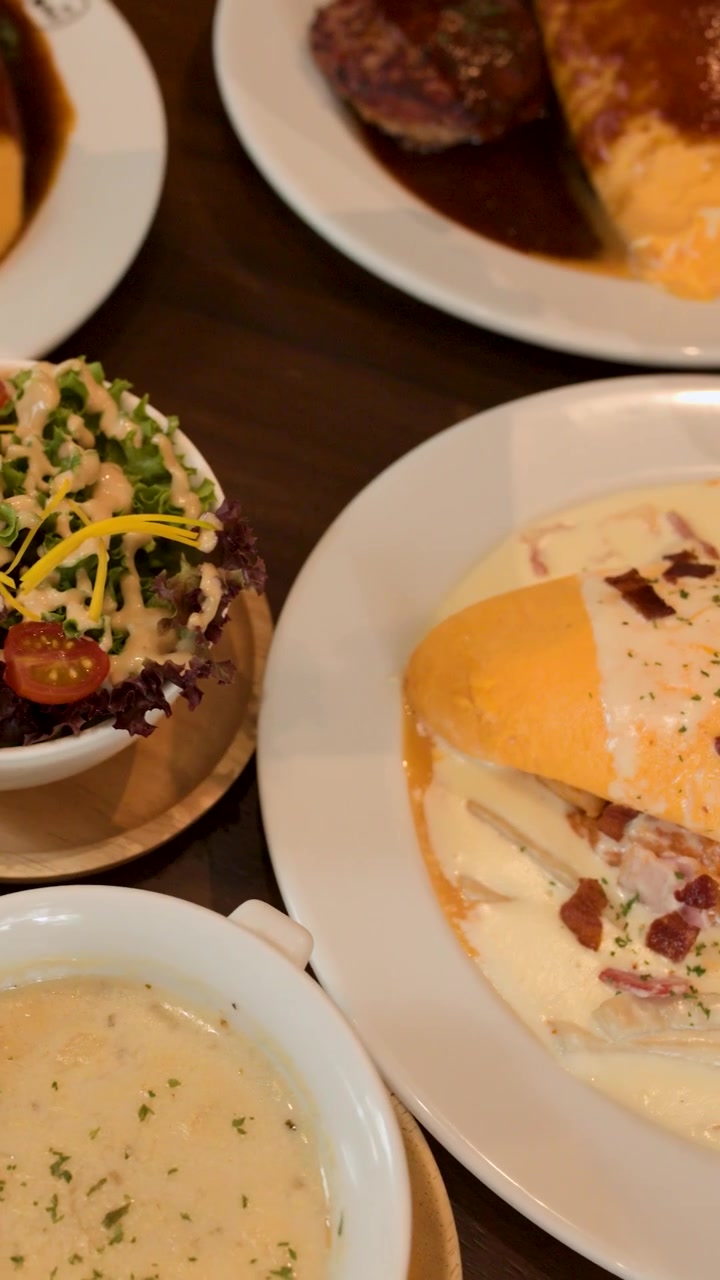 Japanischer Omelettreis, serviert mit cremiger Soße, Suppe, Salat und Wurst bei warmer Restaurantbeleuchtung