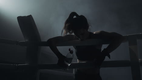 female boxer resting in smoky boxing ring