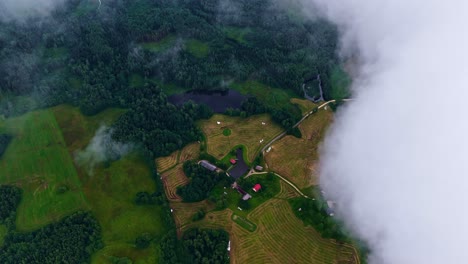 aerial view shows green fields, forests, and a few houses along a winding path - clouds passing in the sky