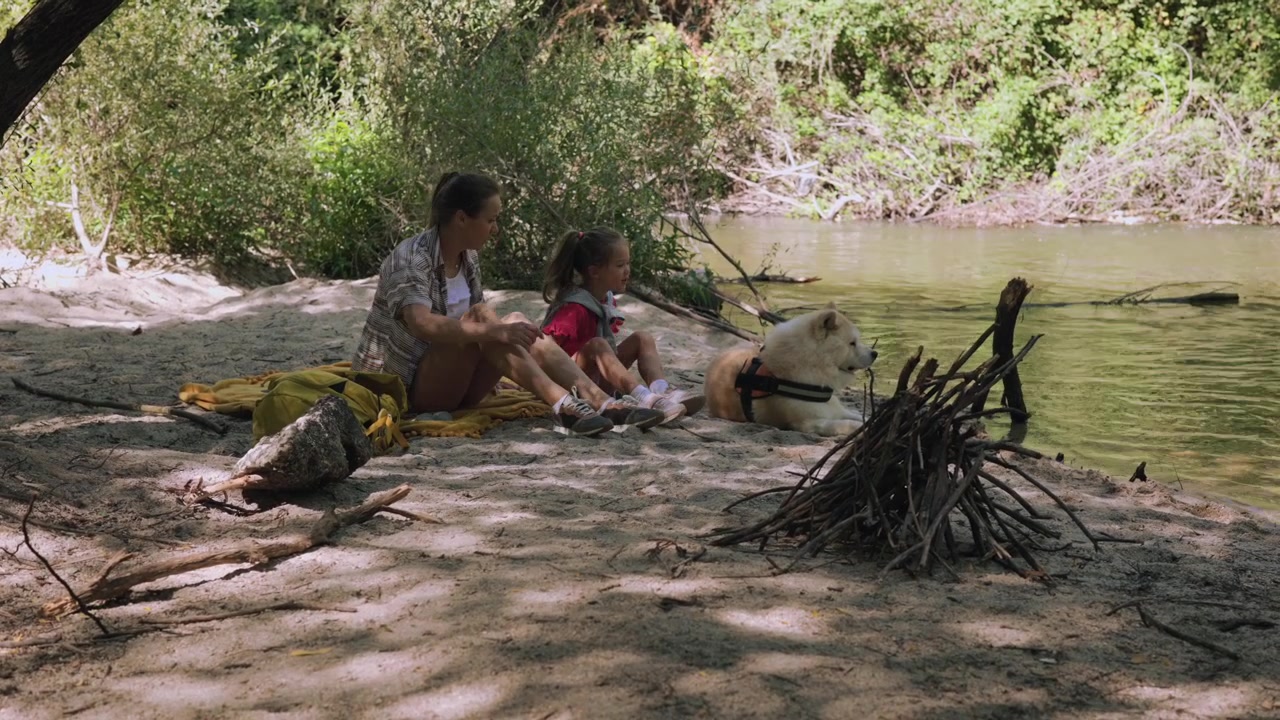 Madre e hija relajándose junto a un río con su perro