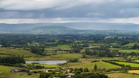 Time-lapse-of-rural-farming-landscape-with-grass-fields,-lake-and-hills-during-a-cloudy-rainy-day-in-Ireland