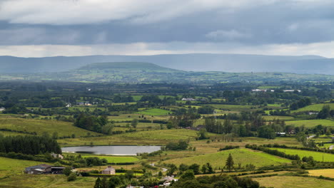 time lapse of rural farming landscape with grass fields, lake and hills during a cloudy rainy day in ireland