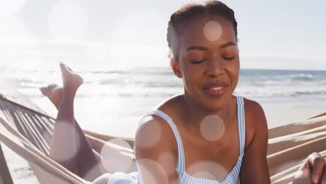 animación de puntos sobre feliz mujer afroamericana en hamaca en la playa