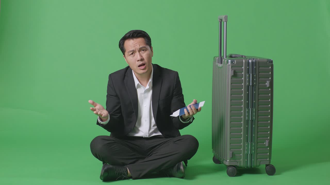 짐을 들고, 여권을 들고, 초록색 스크린을 배경으로 의심스럽게 앉아있는 아시아 사업가 여행자의 신체가 가득 차 있습니다.
