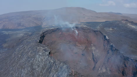 Striking-aerial-view-circling-around-Fagradalsfjall-smoky-crater-cone,-Iceland,-day