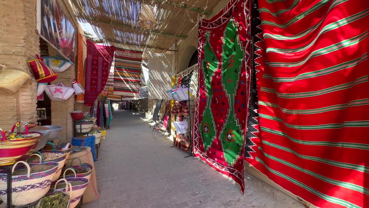 Bright woven rugs hang beside handmade baskets along a narrow covered market alley in Tozeur, Tunisia.