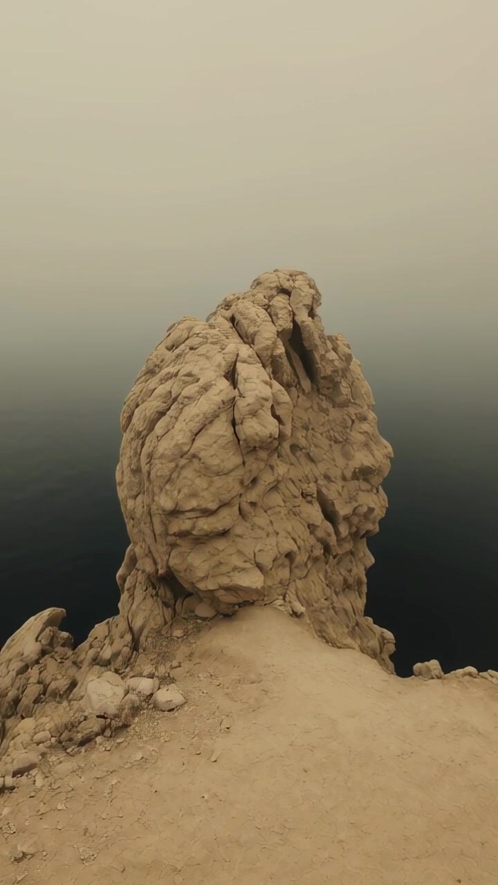 Vertikal video: Et bevægende kamera afslører den højre side af en stor klippe på et sandet plateau og blotlægger en sprække.