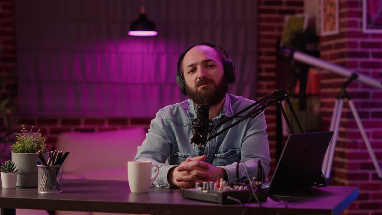 Portrait of man recording podcast using audio mixer and laptop computer talking in professional microphone