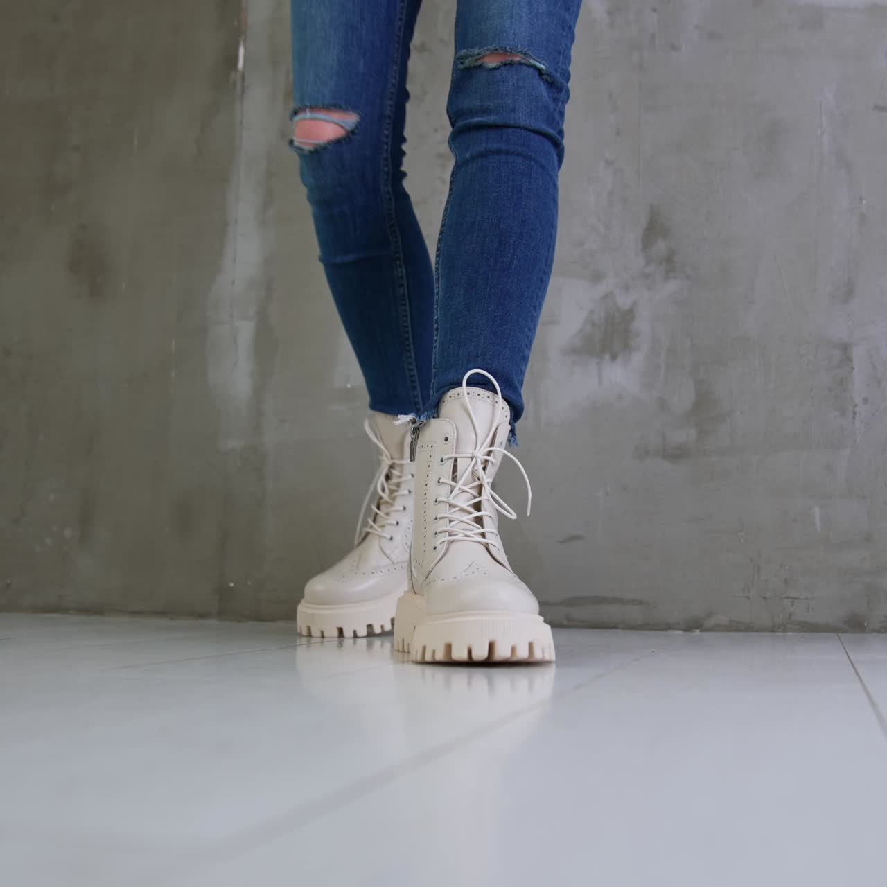 Model in blue jeans shows white boots on tractor soles. Close up. Studio footwear presentation. Low angle view