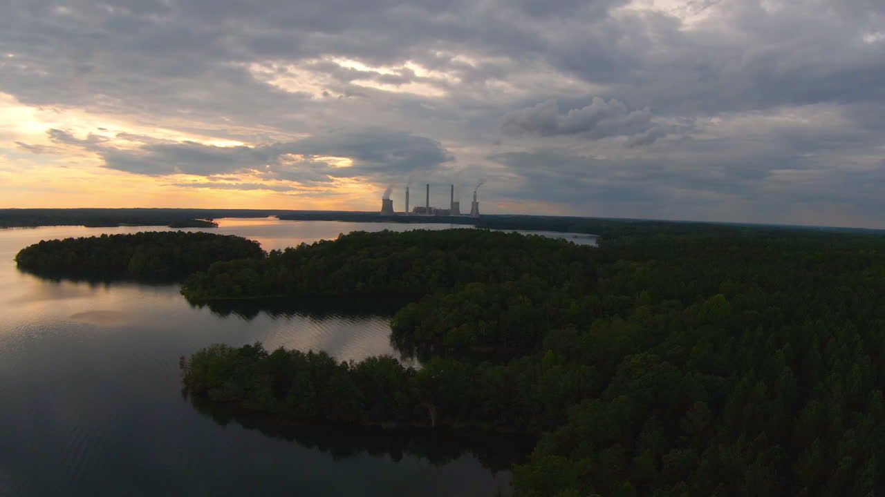 vuelo fpv sobre el lago y el bosque con planta de energía en la distancia durante la hora dorada