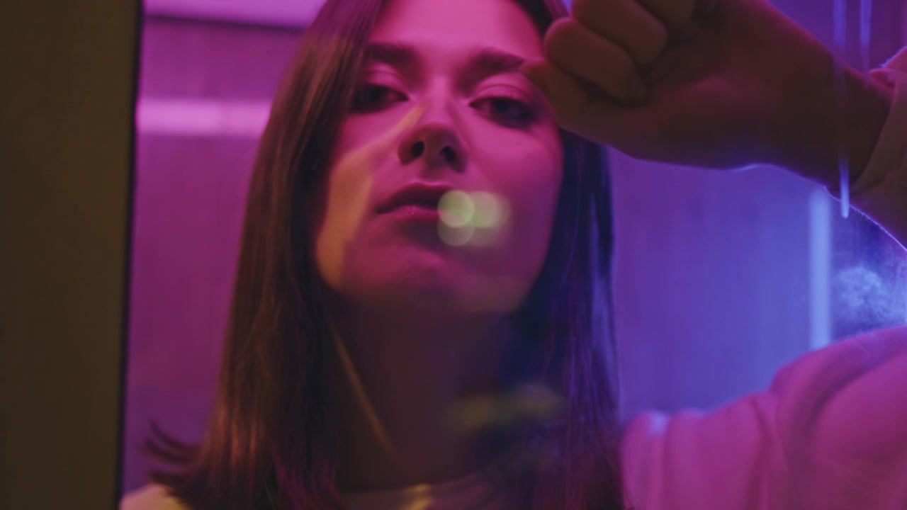 Donna dietro una finestra di vetro con luci al neon in primo piano. Ritratto notturno di ragazza che alza la mano.