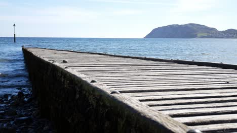 pasarela de madera desgastada que conduce a la reluciente isla de gales del norte olas azules del océano que se elevan tiro derecho
