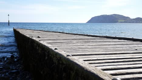 worn wooden boardwalk leading down to shimmering north wales island blue ocean waves rising right shot