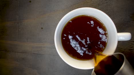 Top-view-of-coffee-being-poured-in-to-white-mug-with-circling-bubbles-and-steam