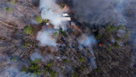 top down aerial footage of a house in the forest with a wildfire burning all around it.