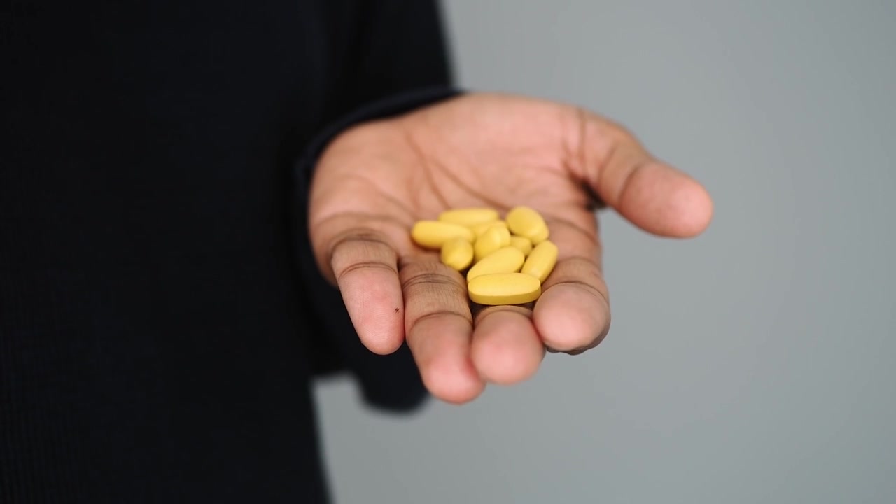 Seseorang Memegang dan Menghitung Pil Kuning di Tangan