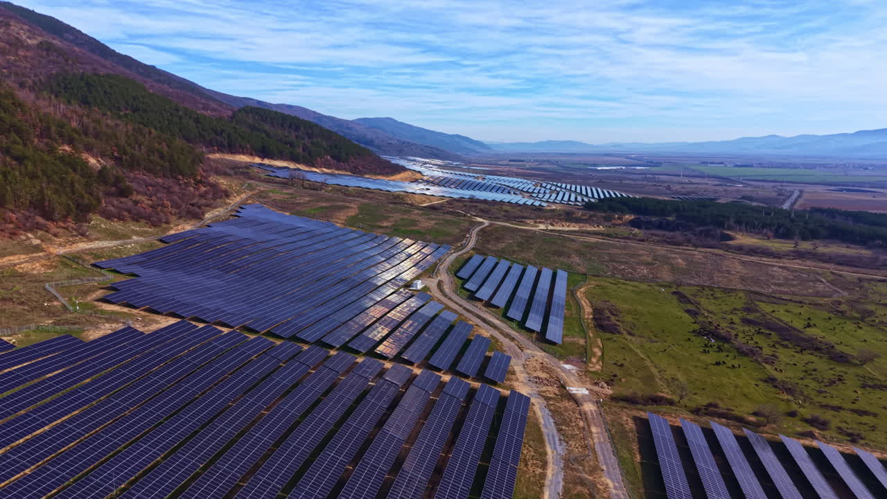 Solpaneler dækker et stort landområde i et anlæg for vedvarende energi i et bjergrigt område om dagen.