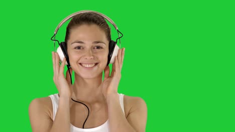 smiling young woman listening to music with headphones on a green screen, chroma key