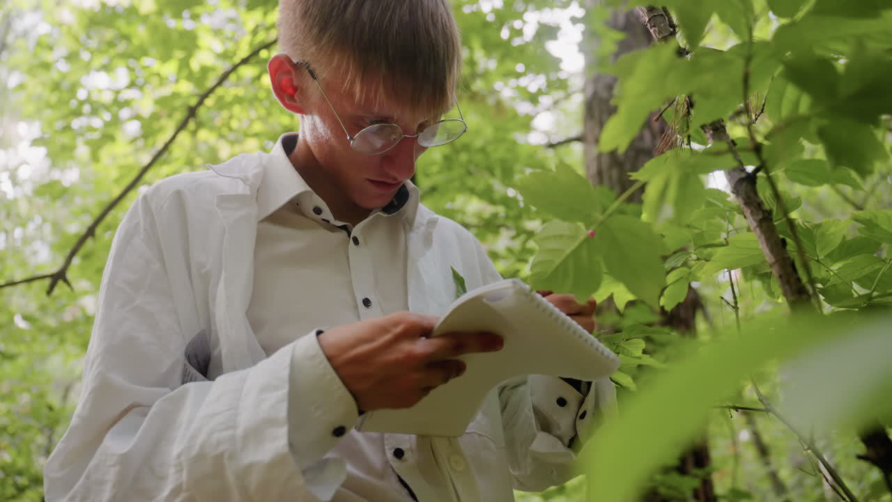Biologist in white coat stands in forest under bright sunlight with serious expression writing notes in jotter using pen, documenting ecological research observations surrounded by lush green leaves