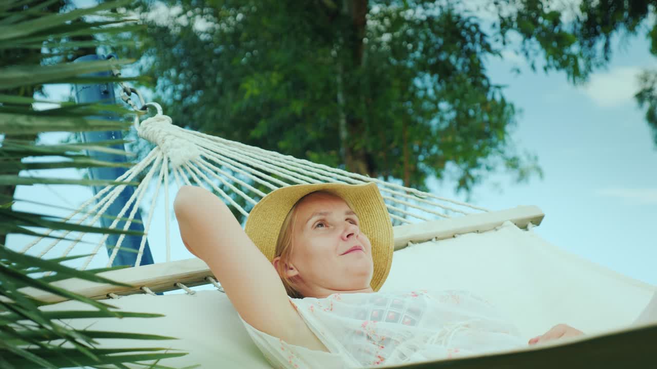 한 젊은 여성이 휴가를 즐기며 해변 리조트에서 햄록에서 휴식을 취하고 있습니다.