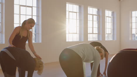 yoga class instructor teaching mature women practicing standing forward bend pose enjoying healthy lifestyle in fitness studio at sunrise