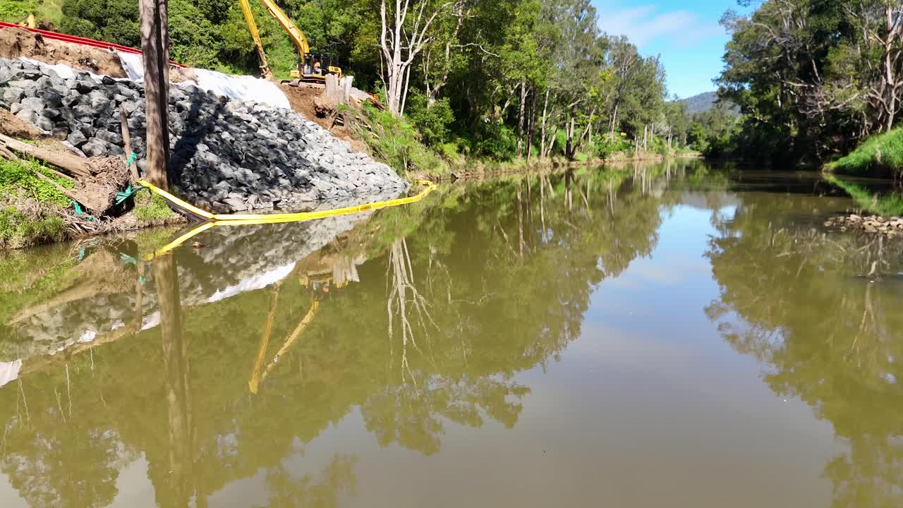 Aerial footage captures riverbank construction with excavator and tractor near Tweed Creek, Uki, under clear skies