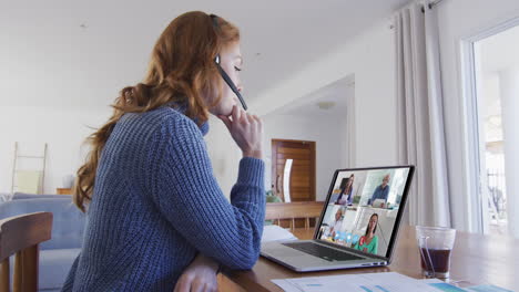 mujer caucásica usando portátil y auriculares de teléfono en videollamada con colegas