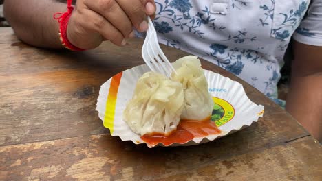 Vista-Frontal-Del-Hombre-Comiendo-Momo-Recién-Horneado-Lleno-De-Carne-Picada-De-Pollo-En-Una-Calle-En-Tiretta-Bazar,-Kolkata,-Con-Un-Tenedor-De-Plástico