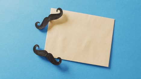 video of two false moustaches and yellow envelope with copy space on blue background