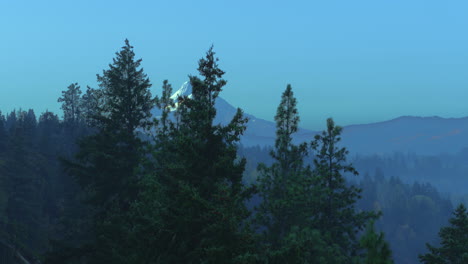 Aerial-rise-up-at-sunrise-with-mist-and-fog-in-the-forest-and-trees-revealing-a-mountain-peak-capped-in-snow-and-autumn-colors-starting-show